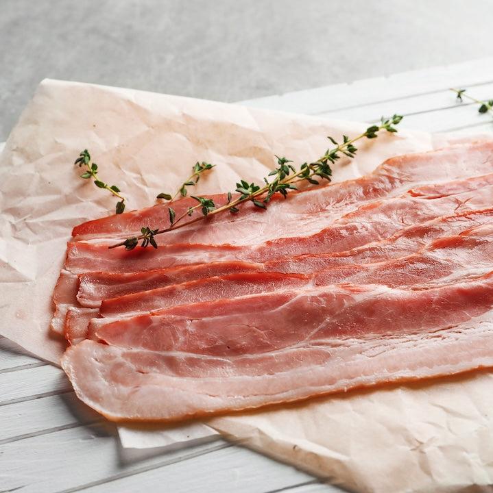 raw bacon slices with sprigs on thyme on parchment paper, sitting on counter.
