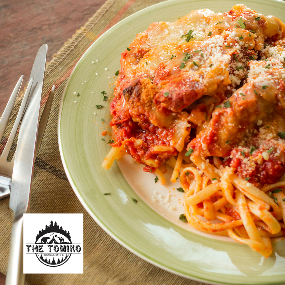 Spaghetti dish with meat sauce on a green plate, featuring The Tomiko logo.