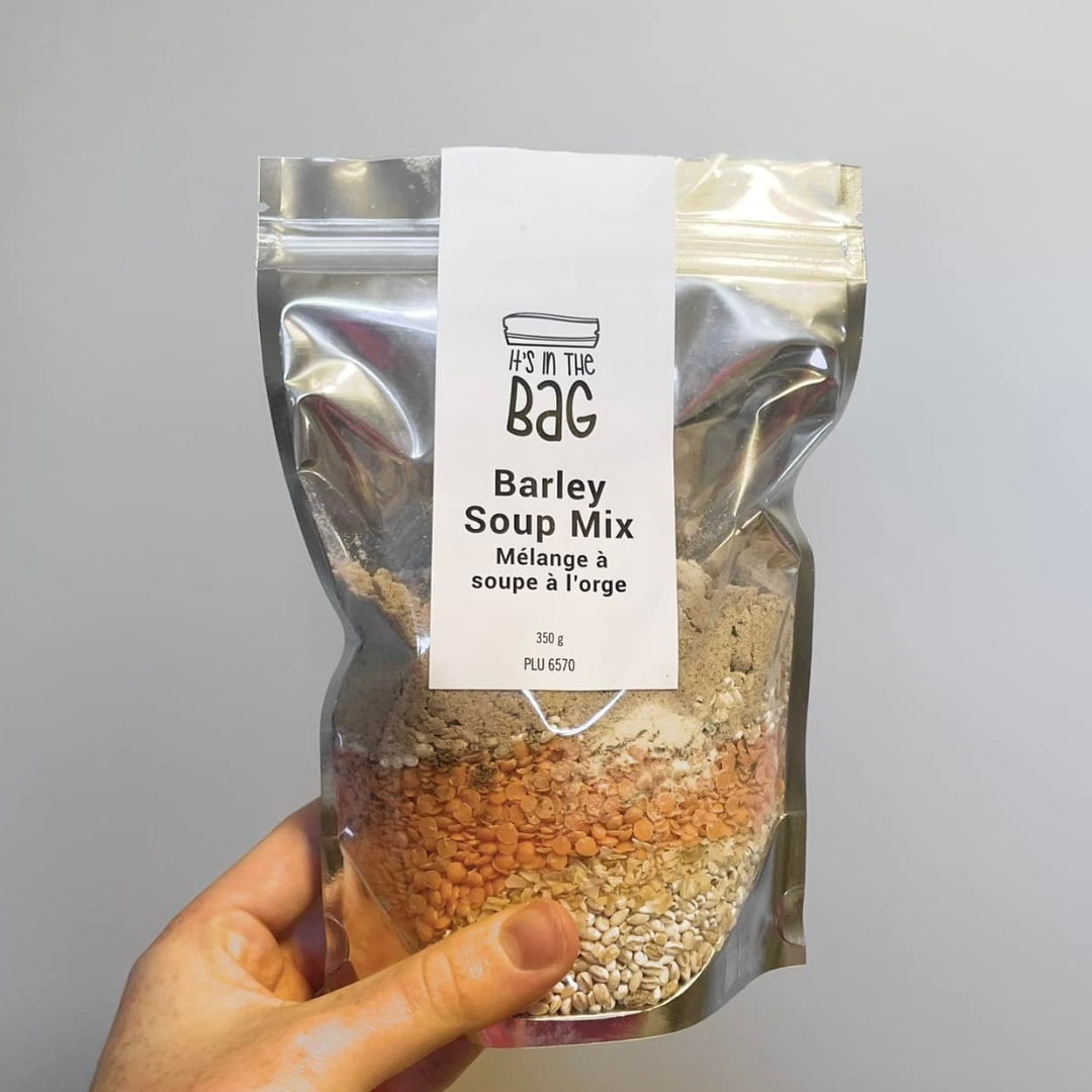 Hand holding a package of barley soup mix with a visible brand label on a gray background