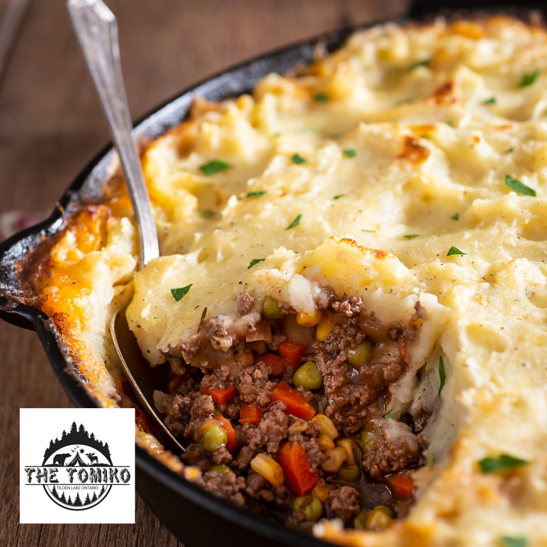 Shepherd's pie with a spoon in a cast iron dish, featuring The Tomiko logo.